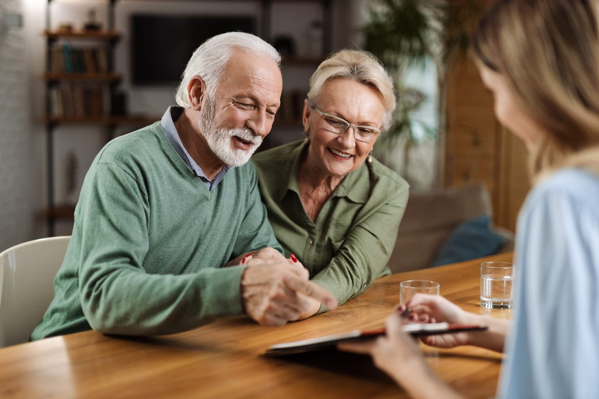 Elderly couple smiling and reviewing a document with another person at a table.