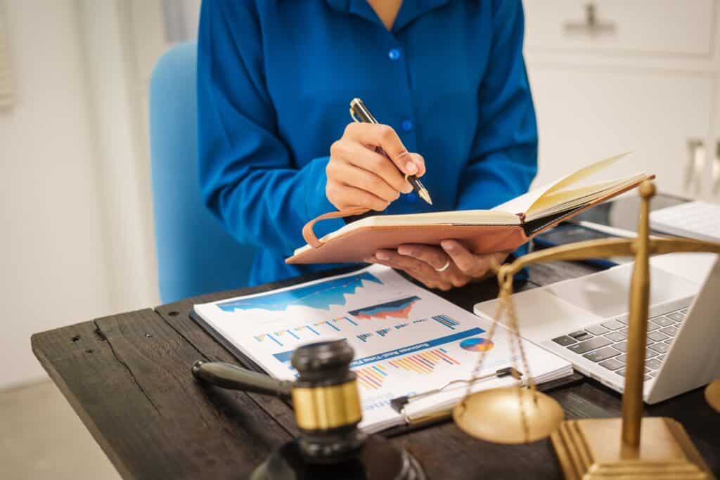An Asian female lawyer sits at her desk in the office,working on legal documents with computer,providing online legal consulting,reviewing contracts,drafting wills,offering signature certification