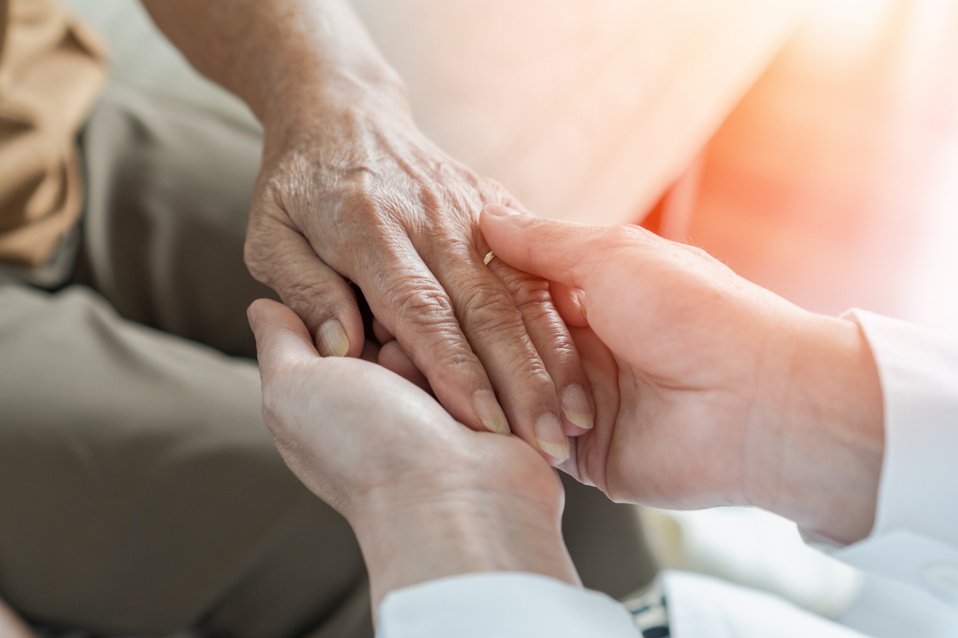 A person holding an elderly person's hand while they sit across from each other.