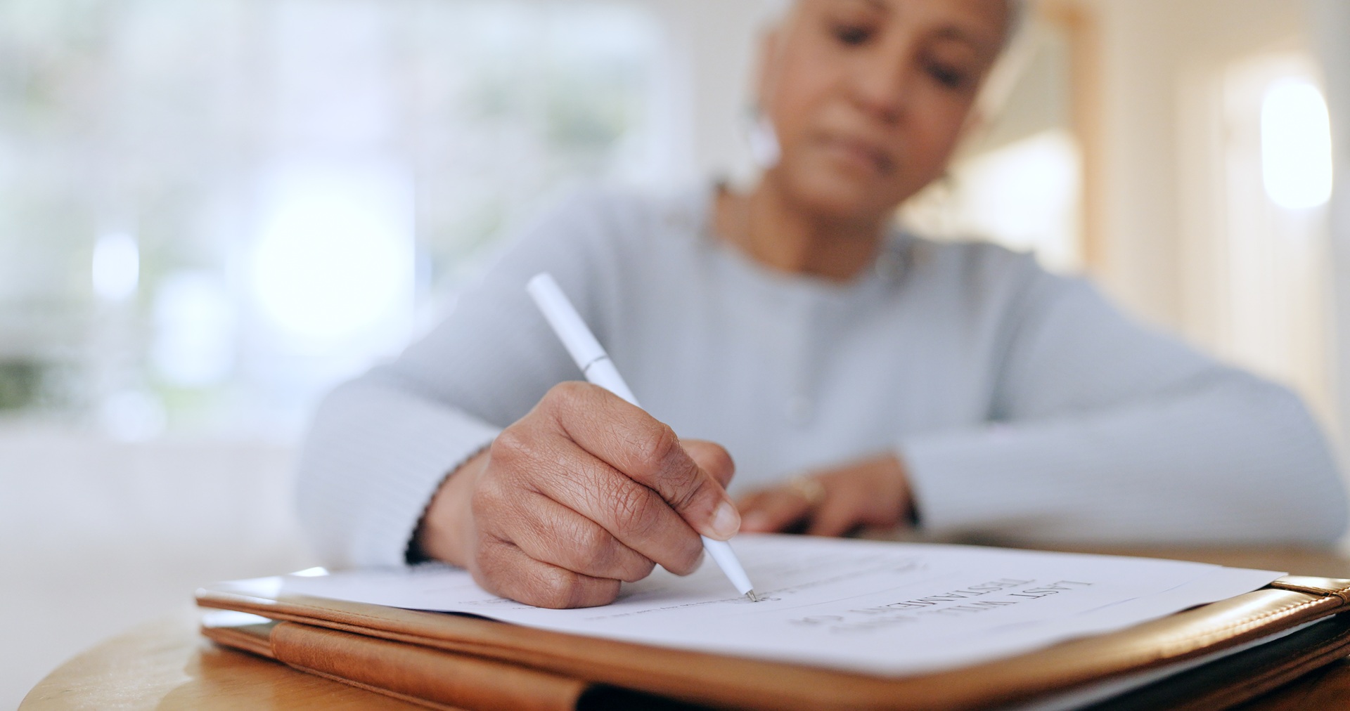 A person with a white pen writing on a piece of paper that's resting on a leather notebook.