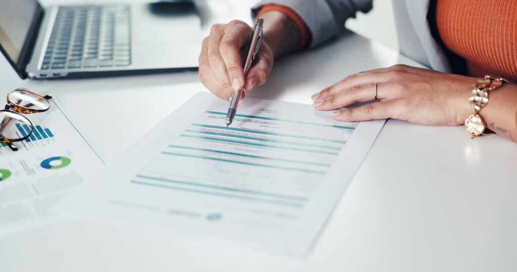 A woman writing on a document with a pen on a white desk.