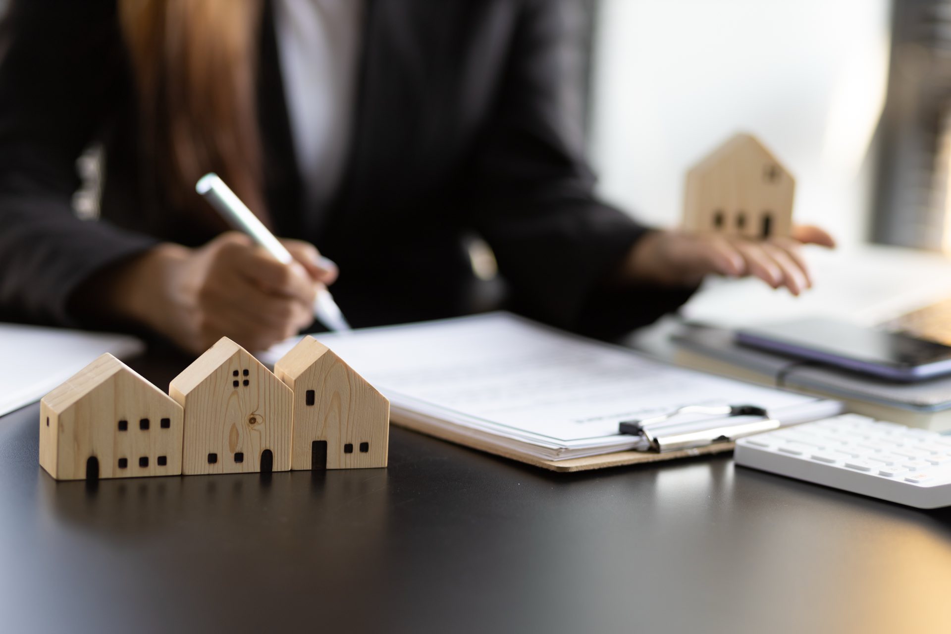 A person sitting at a desk with a pen in their hand in front of paperwork and small wooden houses